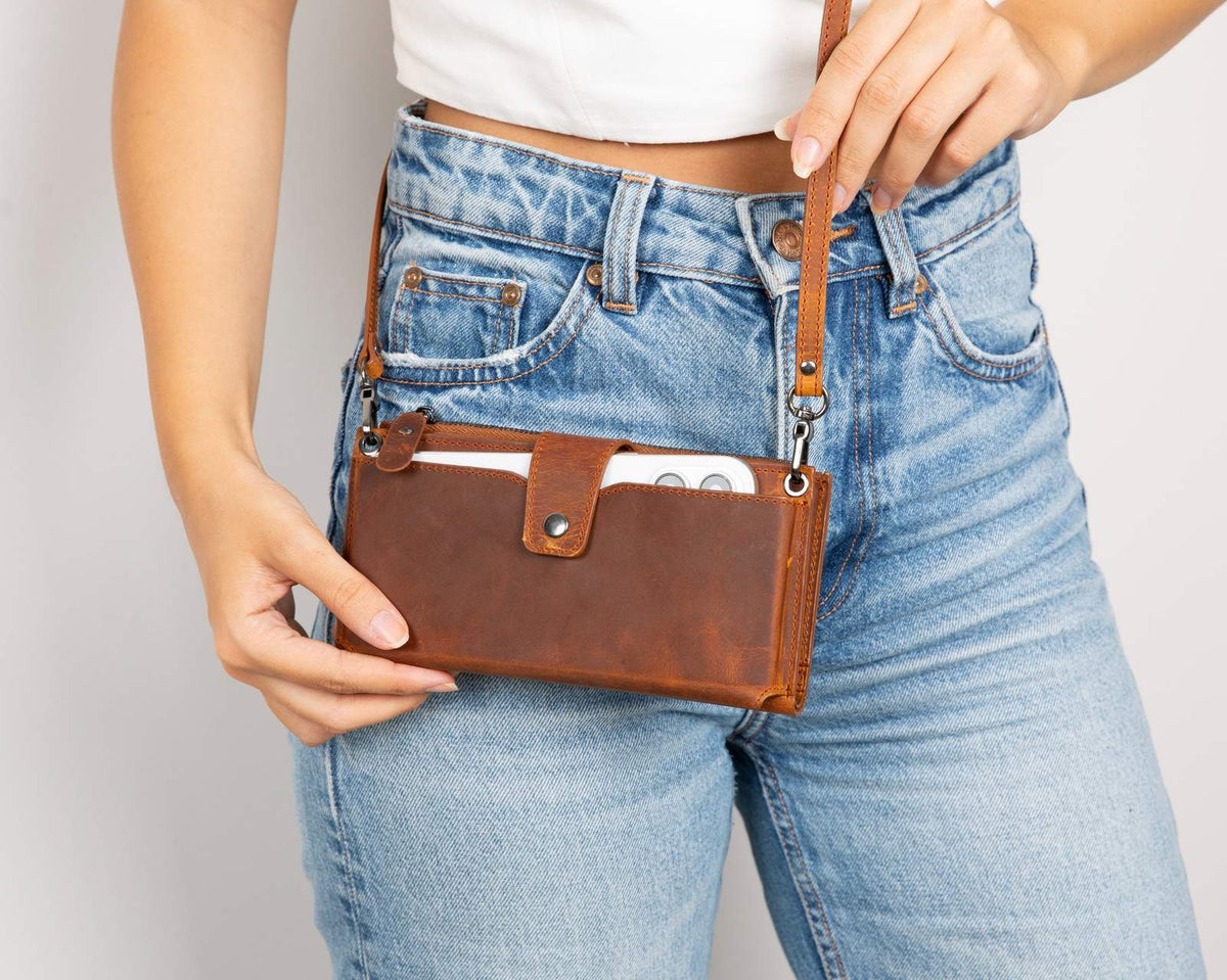 Person wearing a brown leather bag with blue jeans on a plain background