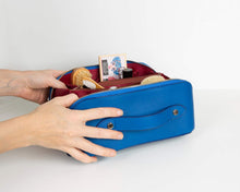 Hands packing cosmetics into a blue leather makeup bag