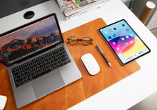 Laptop, tablet, mouse, and glasses on a brown leather desk blotter