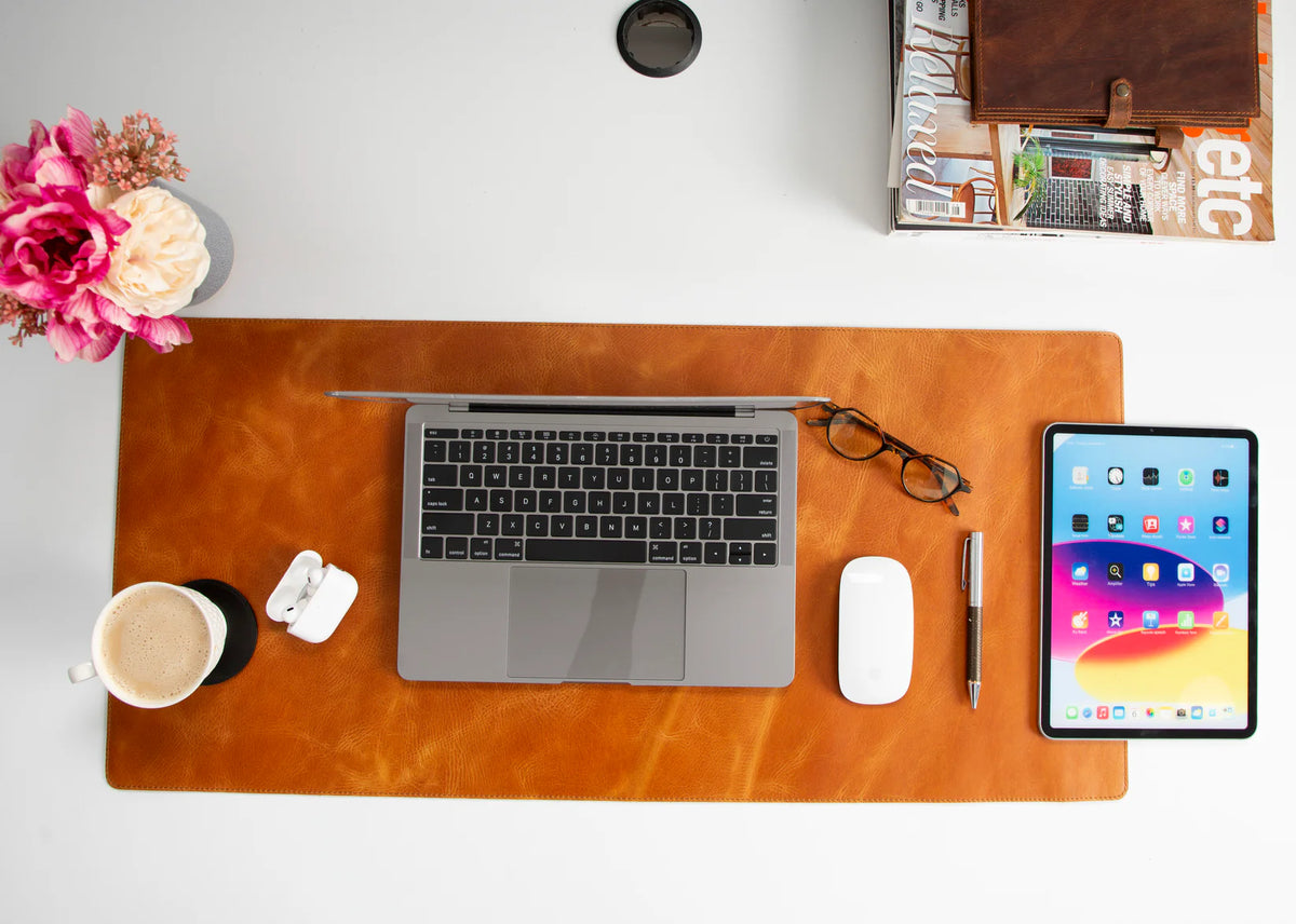 Workstation setup with laptop, tablet, coffee cup, and accessories on a leather desk mat