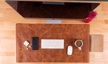 Overhead view of a brown leather desk mat with keyboard, phone and coffee mug.