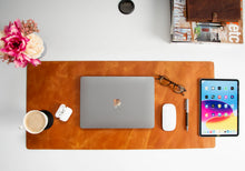 Organized desk with laptop, smartphone, coffee, and flowers on a brown leather desk pad.