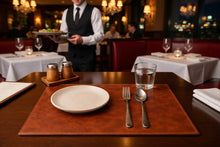 Brown leather placemat with a cream plate and cutlery in a restaurant setting.