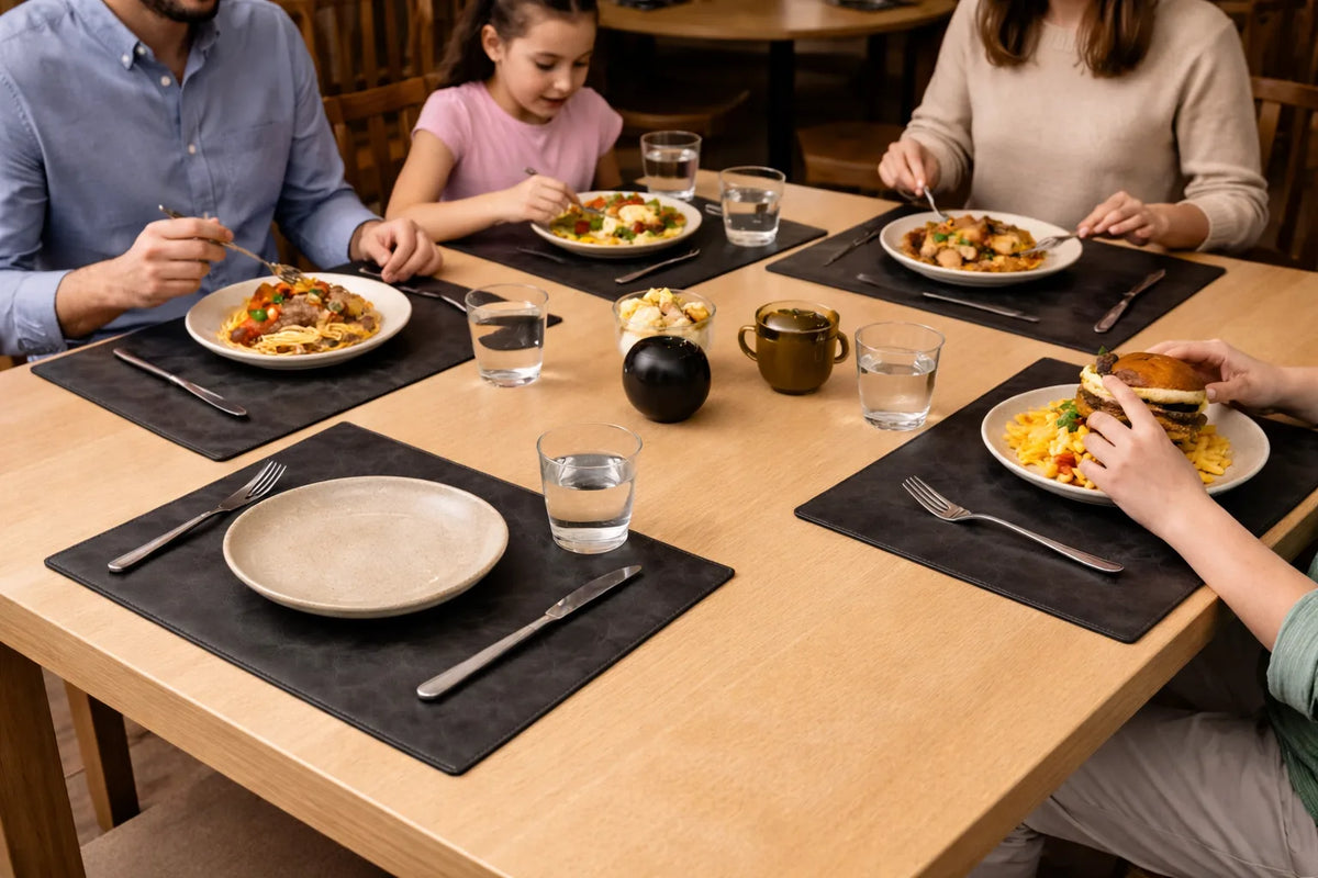 Dark gray leather placemats arranged with plates and cutlery for a family meal.