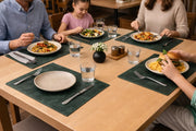 Dark green leather placemats with cream plates and water glasses on a dining table.